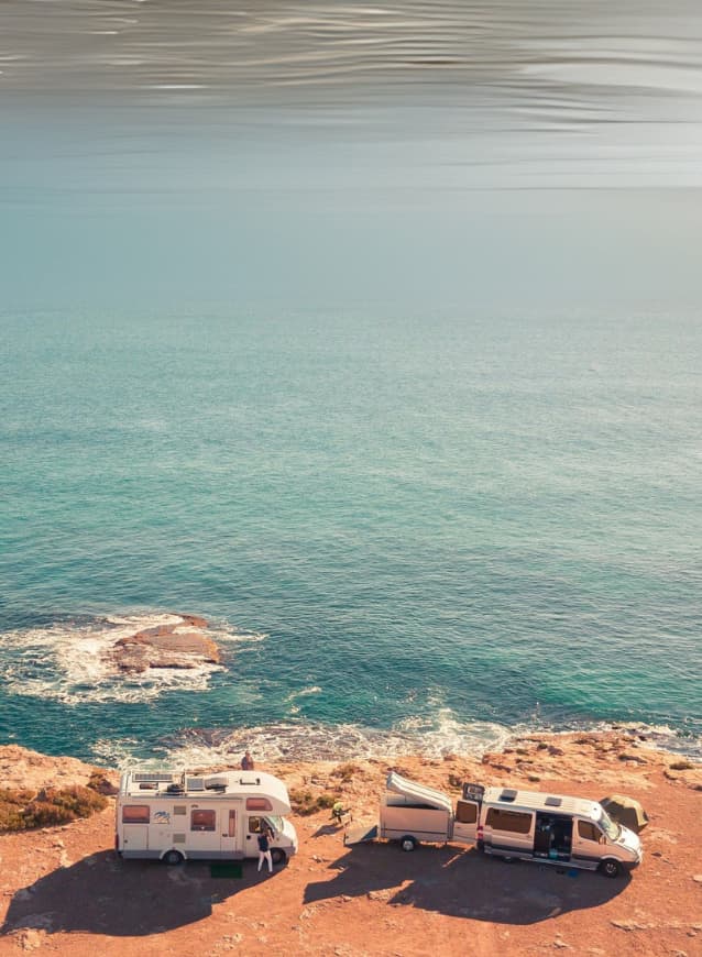 Solar-equipped RVs parked on a remote coastal cliff, showcasing off-grid camping by the ocean under clear blue skies